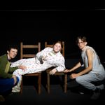'The Heights' by Lisa McGee, performed by St Brendan's Sixth Form College. Two young people crouched down beside one young person in a dressing gown lying on a pair of chairs.