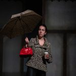'Samphire' by Shamser Sinha, performed by Aberystwyth Arts Centre Youth Theatre. A young person in a leopard print jacket, with a matching umbrella, a disposable coffee cup, and a red handbag.