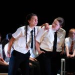 'Strangers Like Me' by Ed Harris performed by Crescent Arts Youth Theatre, Belfast. Young people dressed in school uniform. One is leaning on the other with eyes closed and teeth bearing. The other young person listens.