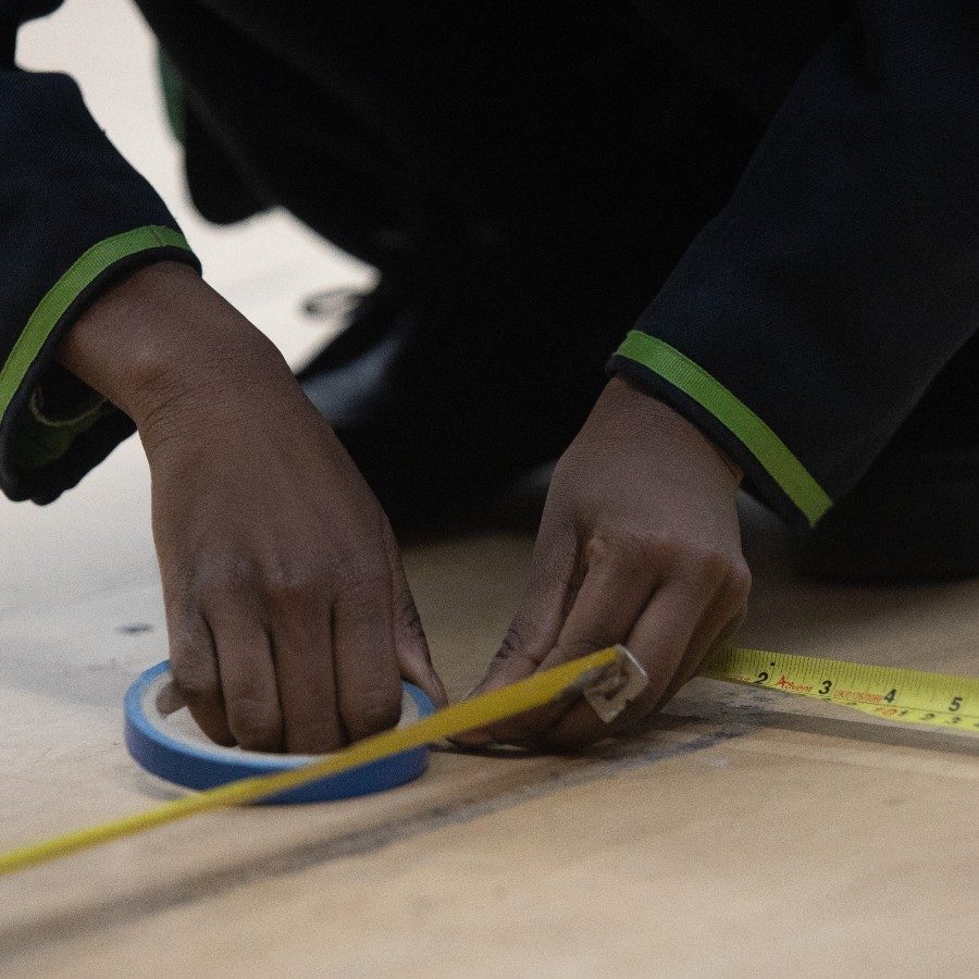 A pair of hands marking up a floor with measuring tape.