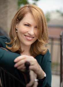 A woman with auburn hair smiling and wearing an olive green top