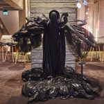 A black floor-length costume, made with a variety of materials, totally covering the face and with protuberances from the sides