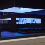 Model box showing a rectangular cube with long windows through which you can see chairs, a table and some model people