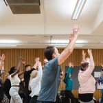 A large group of teachers with their hands in the air, taking part in a Drama Teacher Conference movement workshop 2023