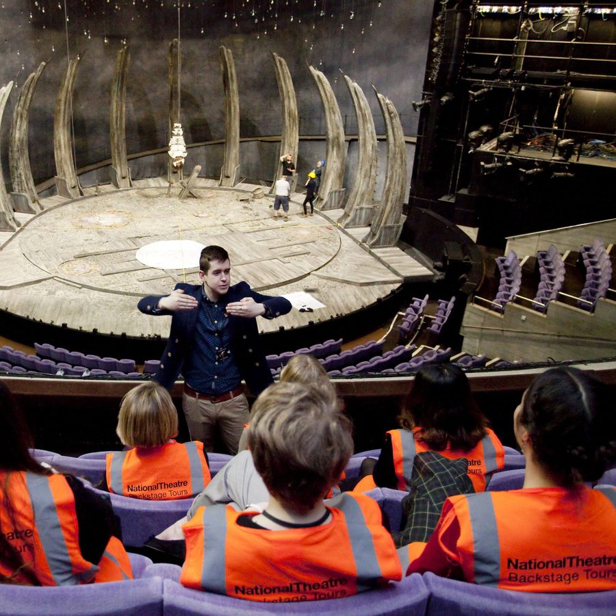 A tour guide talking to a tour group in the Olivier theatre auditorium. The tour participants wearing orange high-visibility vests.