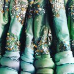 A row of jacket sleeves in shades of blue and green, all with sequins at the shoulders and above the cuffs.