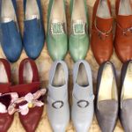 Six pairs of old fashioned shoes, three with buckles, one with a bow and all made bright coloured material.