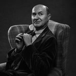 A black and white portrait photo of a Mark Gatiss sitting in an arcmchair, looking slightly away from the camera.
