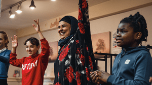 A woman in a headscarf with two young people either side of her with their hands in the air